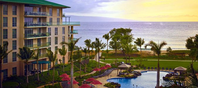 A large hotel with a pool and beach, beautifully illuminated by the warm hues of sunset in the background.