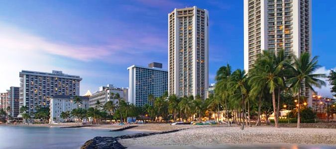 A beach with palm trees and buildings in the background.