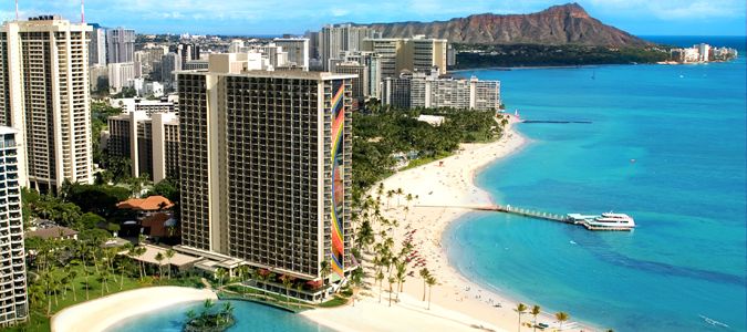 A vibrant beach scene featuring tall buildings alongside a serene blue ocean under a clear sky.