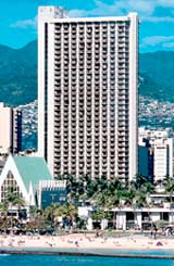 Honolulu hotels: High-rise building dominating the skyline along a beachfront with a backdrop of mountains.