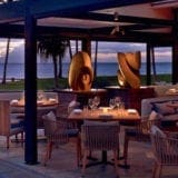 Oceanfront restaurant at dusk with an elegant dining setup and contemporary art sculptures.