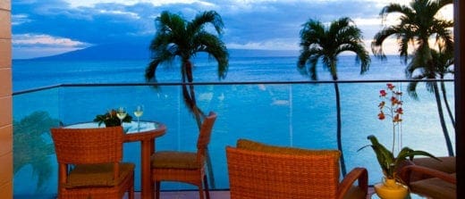 Balcony with ocean view, featuring a table set for two and tropical palm trees.