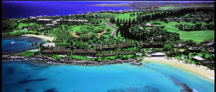 Aerial view of a coastal landscape with lush greenery, winding roads, and clear blue waters.