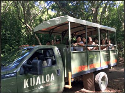 A group of individuals enjoying a ride in a truck, with a visible sign reading "Kualoa Ranch" in the background.